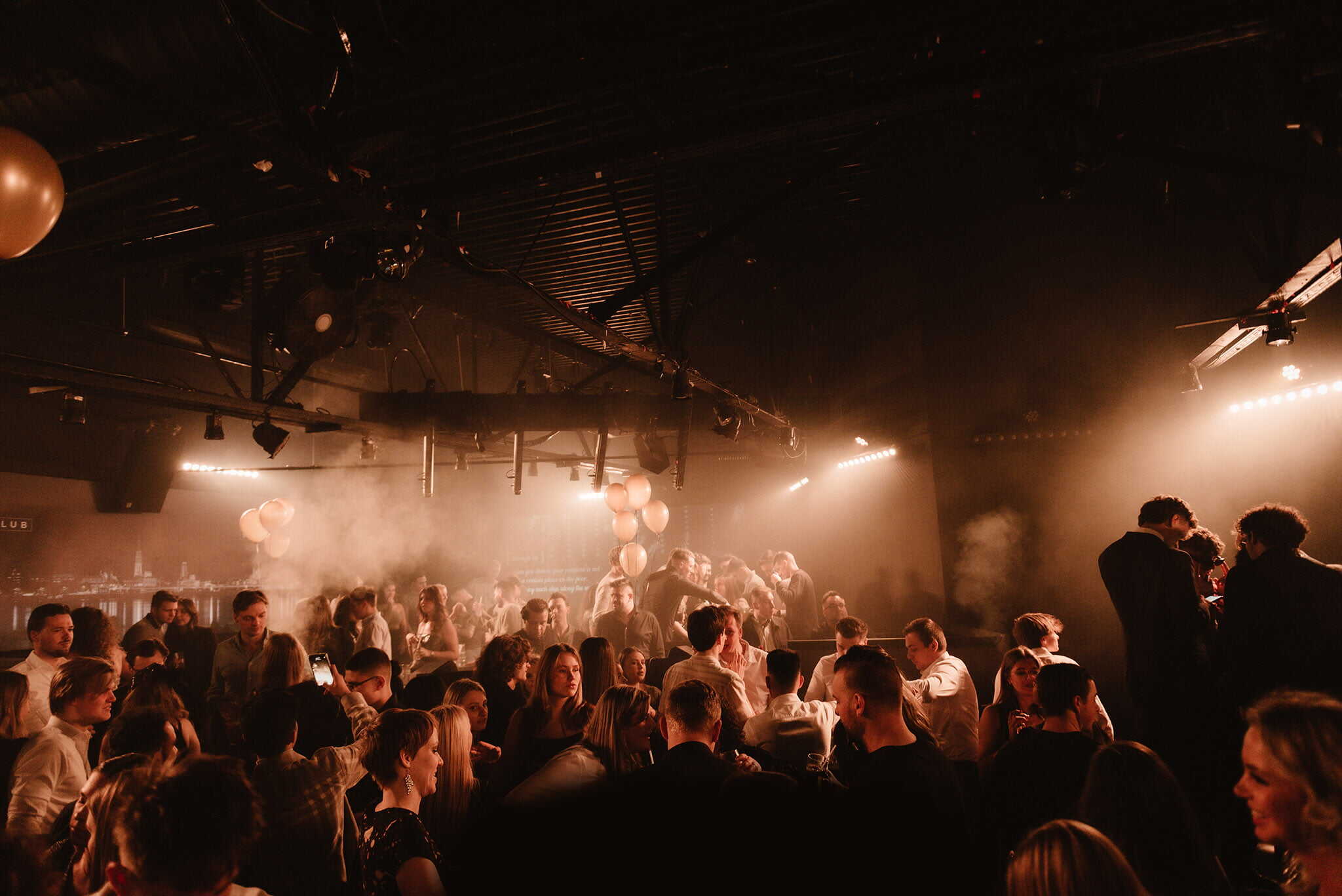 Een bruisend nachtleven met een dansvloer vol feestvierders in een sfeervol clubgebouw, verlicht door warme lichten en mist, voor een onvergetelijke ervaring in IKON Antwerpen.